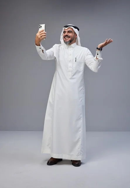 Saudi man in traditional attire taking a selfie with smartphone