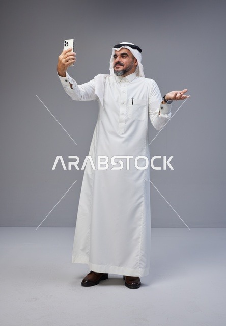 رجل سعودي بالزي التقليدي يلتقط صورة سيلفي بهاتف ذكي