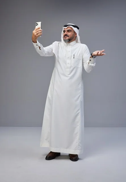 رجل سعودي بالزي التقليدي يلتقط صورة سيلفي بهاتف ذكي