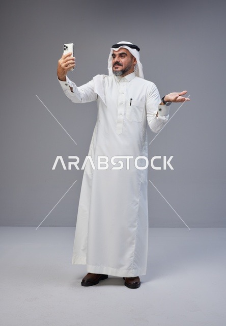 رجل سعودي بالزي التقليدي يلتقط صورة سيلفي بهاتف ذكي