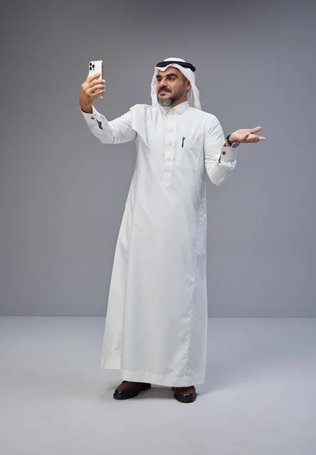Saudi man in traditional attire taking a selfie with smartphone