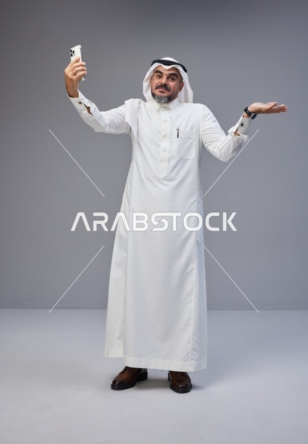 رجل سعودي بالزي التقليدي يلتقط صورة سيلفي بهاتف ذكي