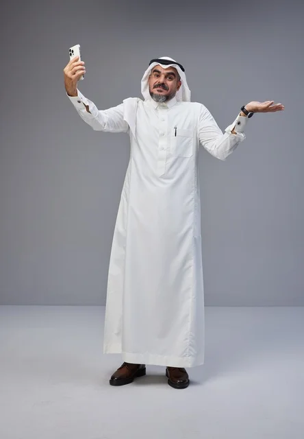 Saudi man in traditional attire taking a selfie with smartphone