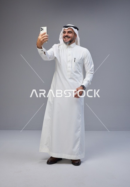 رجل سعودي بالزي التقليدي يلتقط صورة سيلفي بهاتف ذكي