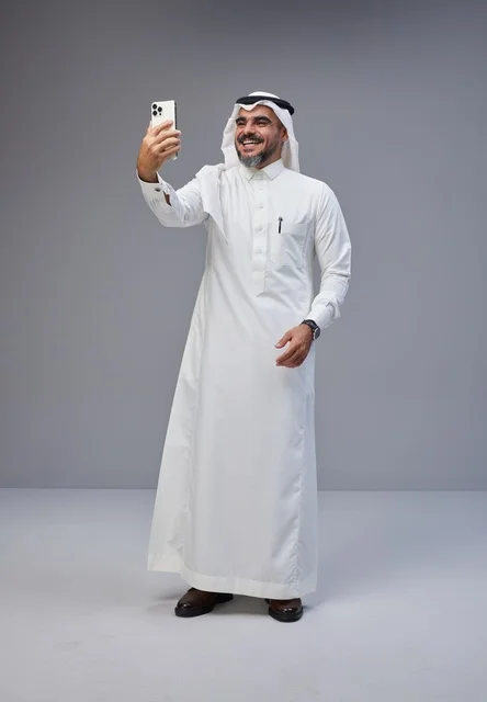 رجل سعودي بالزي التقليدي يلتقط صورة سيلفي بهاتف ذكي