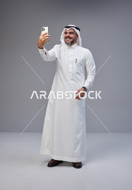 رجل سعودي بالزي التقليدي يلتقط صورة سيلفي بهاتف ذكي