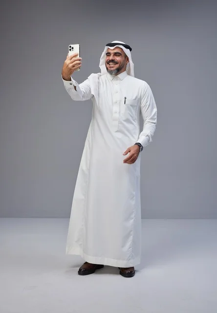 رجل سعودي بالزي التقليدي يلتقط صورة سيلفي بهاتف ذكي