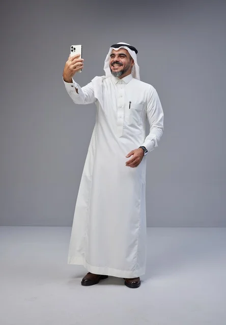 رجل سعودي بالزي التقليدي يلتقط صورة سيلفي بهاتف ذكي