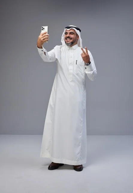 Saudi man in traditional attire taking a selfie with smartphone