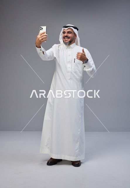 رجل سعودي بالزي التقليدي يلتقط صورة سيلفي بهاتف ذكي