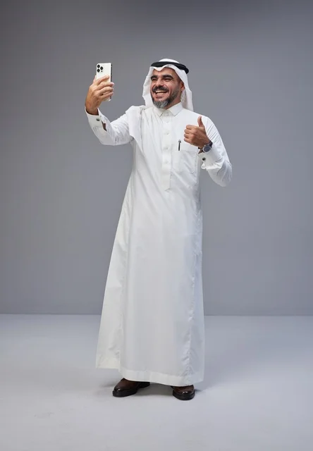 Saudi man in traditional attire taking a selfie with smartphone