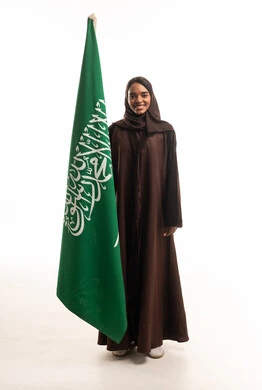 امرأة سعودية بعباءة بنية مع العلم الوطني