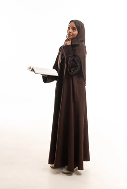 امرأة سعودية بعباءة بنية تمسك كتاباً وتفكر