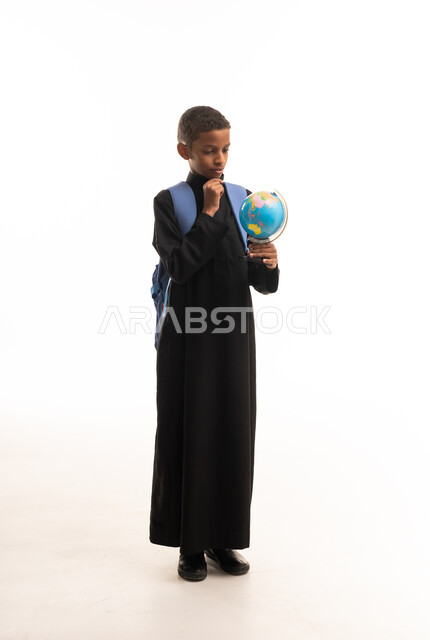 طالب سعودي بالثوب الأسود يحمل مجسم الكرة الأرضية بخلفية بيضاء
