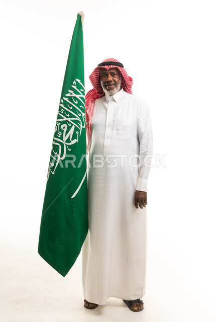 رجل سعودي مسن يقف بجانب العلم الوطني السعودي خلفية بيضاء