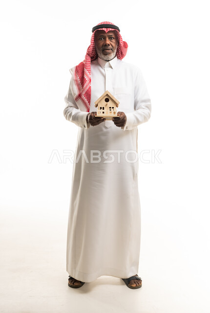 رجل سعودي مسن يحمل مجسم منزل خشبي