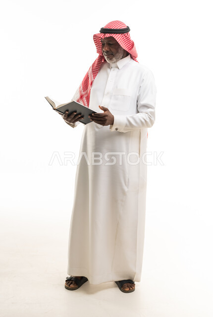 رجل سعودي مسن يقرأ كتاباً بالزي التقليدي