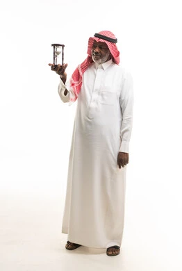 رجل سعودي مسن يحمل ساعة رملية بالزي التقليدي