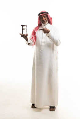 رجل سعودي مسن يحمل ساعة رملية بخلفية بيضاء