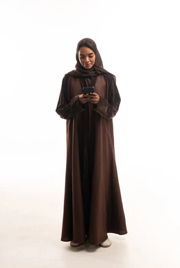 امرأة إماراتية بعباية بنية تستخدم الهاتف الذكي