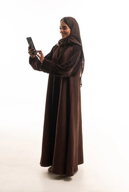 امرأة سعودية بعباءة بنية تستخدم الهاتف الذكي
