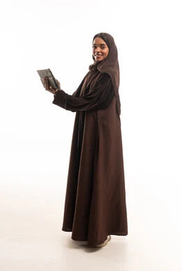 امرأة سعودية بعباءة بنية تحمل جهاز لوحي في الاستوديو