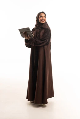 امرأة سعودية بعباءة بنية تحمل جهازاً لوحياً خلفية بيضاء