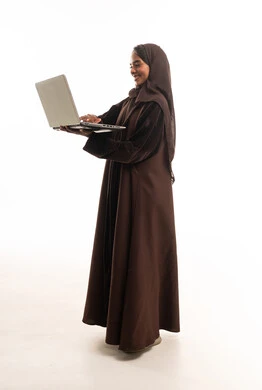 امرأة سعودية بعباية بنية تستخدم لابتوب خلفية بيضاء