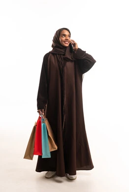 امرأة سعودية تحمل حقائب تسوق وتستخدم الهاتف الذكي