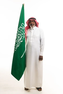 رجل سعودي مسن يحمل العلم السعودي في استوديو أبيض