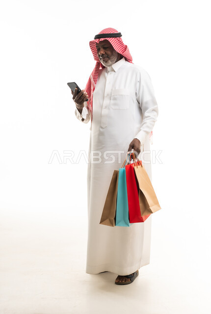 رجل سعودي مسن مع حقائب تسوق وهاتف ذكي