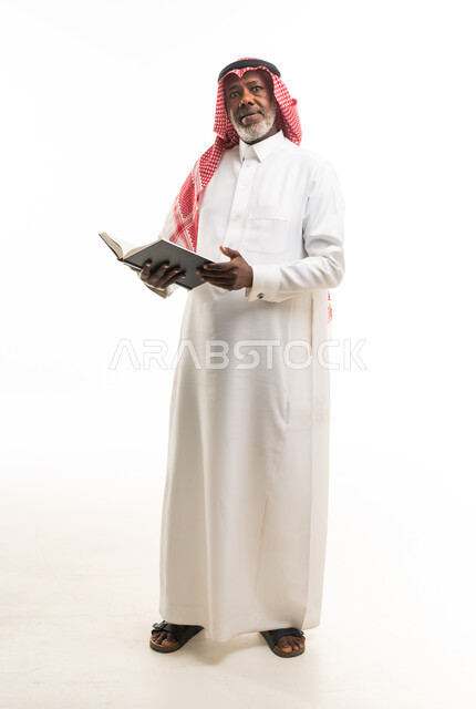 رجل مسن يرتدي الثوب السعودي يحمل كتاباً