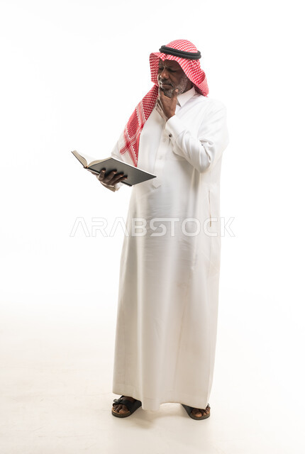 رجل سعودي مسن يقرأ كتاباً بتركيز على خلفية بيضاء