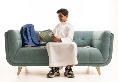 طالب سعودي بالثوب الأبيض يقرأ على الأريكة