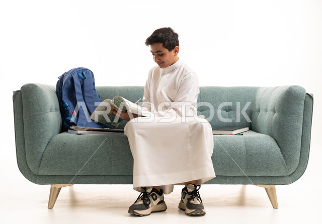 طالب سعودي بالثوب الأبيض يذاكر على الأريكة