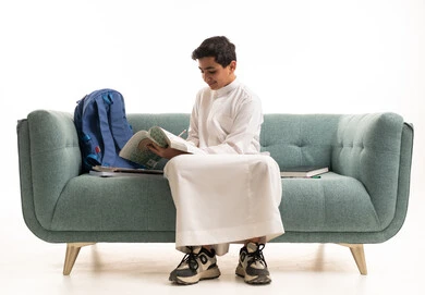 طالب سعودي بالثوب الأبيض يذاكر على الأريكة