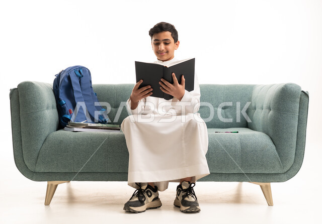 طالب سعودي بالثوب التقليدي يقرأ كتاباً على الأريكة