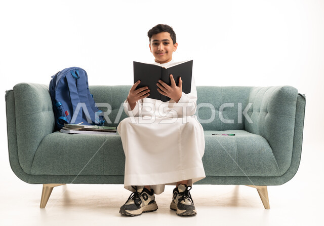 Saudi Boy in White Thobe Reading Book on Green Sofa