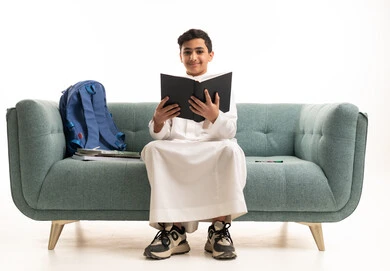 Saudi Boy in White Thobe Reading Book on Green Sofa