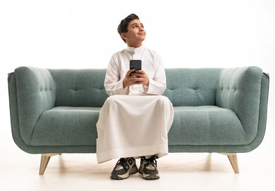 Saudi Boy in White Thobe Using Smartphone on Sofa