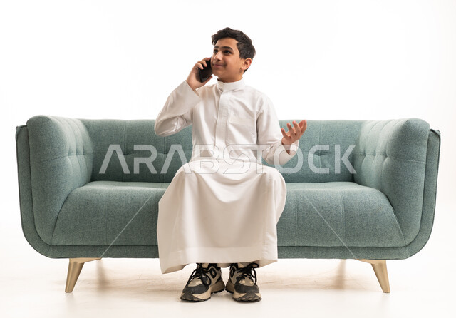 شاب سعودي بالثوب التقليدي يتحدث بالجوال على الأريكة