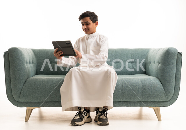 فتى سعودي يستخدم جهازاً لوحياً على أريكة خضراء