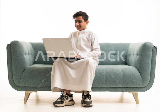 فتى سعودي يستخدم المحمول على الأريكة بخلفية بيضاء