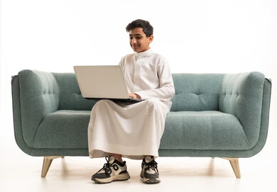 Saudi Boy Using Laptop on Sofa White Background