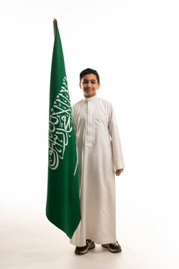 فتى سعودي يحمل علم المملكة بالثوب التقليدي