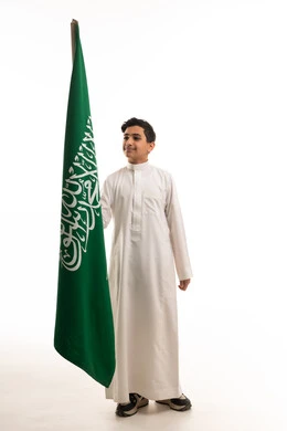 صبي سعودي يرتدي الثوب التقليدي ممسكا بعلم السعودية