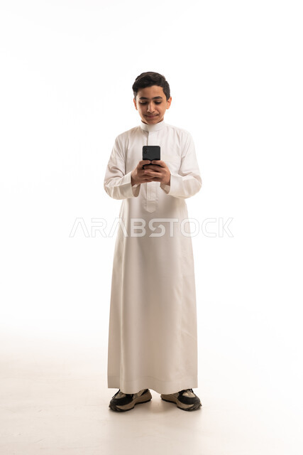 فتى سعودي بالثوب الأبيض يحمل هاتف ذكي في الاستوديو