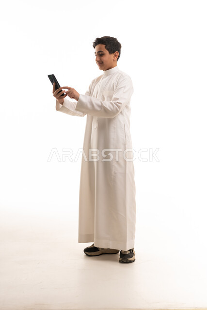 ولد سعودي يرتدي الثوب التقليدي يستخدم الهاتف الذكي