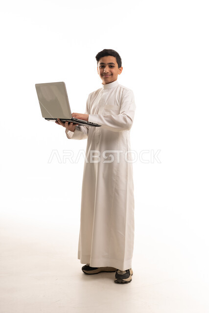 صبي سعودي بالثوب يستخدم الحاسوب المحمول خلفية بيضاء