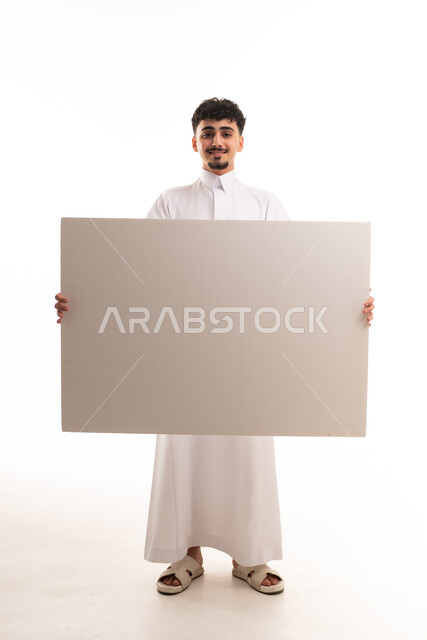 شاب سعودي بالثوب التقليدي يحمل لوحة بيضاء فارغة